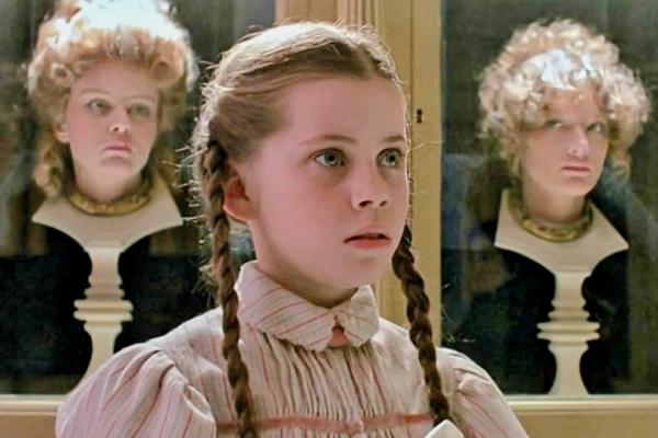 Picture of Dorothy Gail looking shocked. She has stood in front of cabinets filled with young women's heads mounted on plinths.
