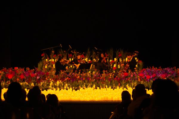A room filled with candles and flowers where an audience watches a live music performance