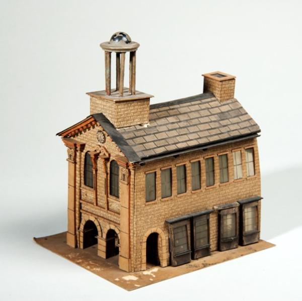 A scale model of a moot hall or meeting house, based on the 1711 Leeds Moot Hall. A pilastered frontage, 2 archways 2 windows a statue and a clock; to one side, shops windows, and an upper storey of 8 sash windows, On the tiled roof is (a dome or cupola) and a chimmney.