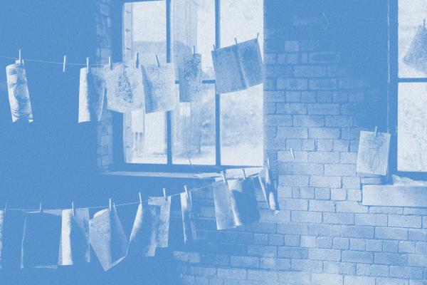 Cyanotype depicting a washing line filled with prints strung between a brick wall and large windows