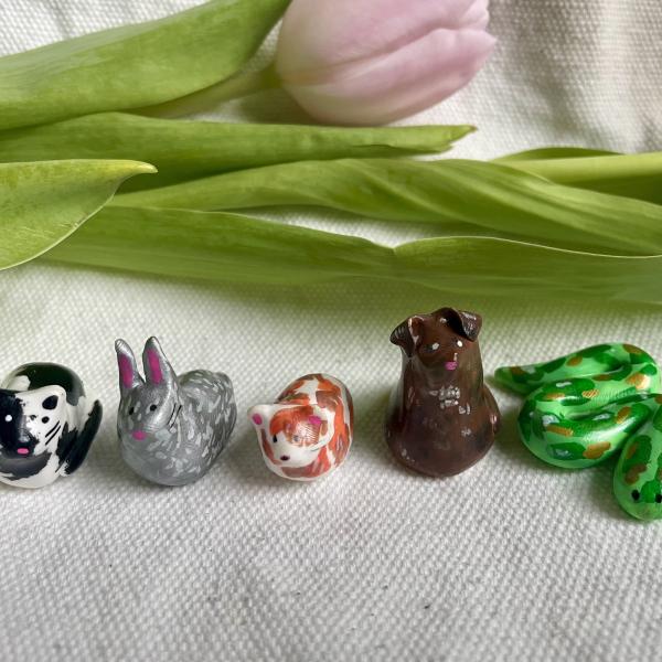 5 polymer clay pets rest on a beige cloth with a tulip behind.