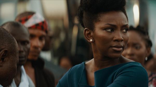 A young Black woman looking in the distance, with other people in the background