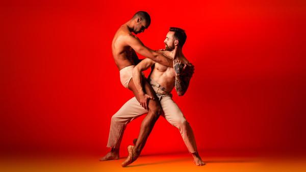 Two men in a dance pose against a red background