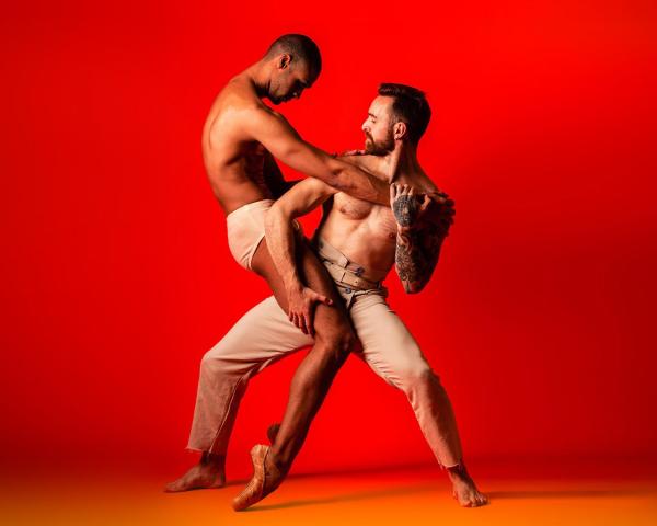A red background with two performers pose in a striking embrace