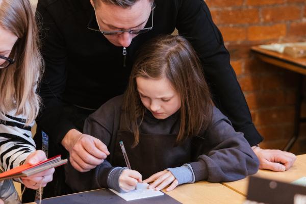 child sat a table drawing parent is assisting