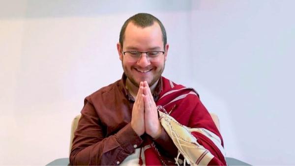 Buddhist Teacher David Oromith, smiling with his hands in prayer pose and wearing his teachers shawl.