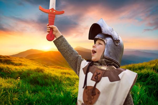 Young child dressed as a knight holds toy sword aloft