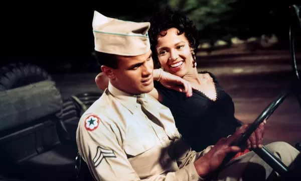 Two people - one in military uniform - sat together in an army jeep.