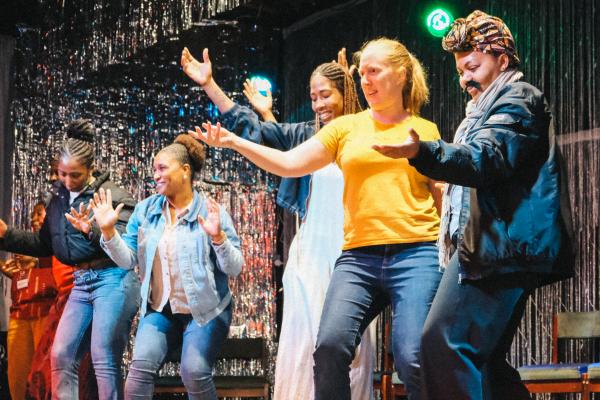 Women share a joyful moment together, dancing and laughing, during a Kuluhenna Drama session