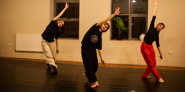 3 dancers leaning to the left with their arms extended over their heads
