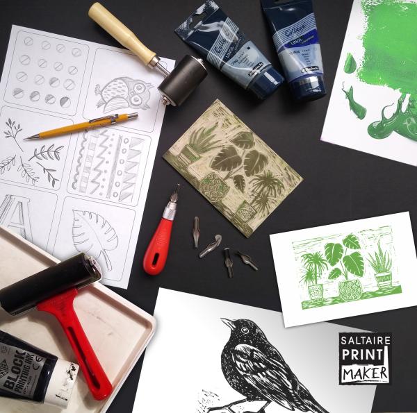 Black desktop featuring mono prints and other tools and inks for making lino prints