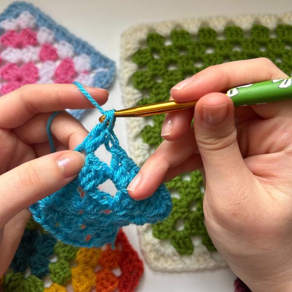 Two hands crocheting a blue granny square