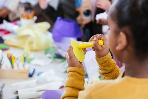 YOUNG PERSON HOLDING A YELLOW PAINT STICK PAINTING AN EGG SHAPED PEACE OF PAPER