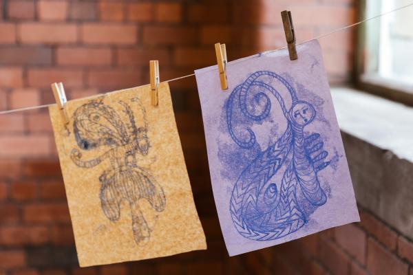 2 mono prints hang from a washing line in front of a red brick wall