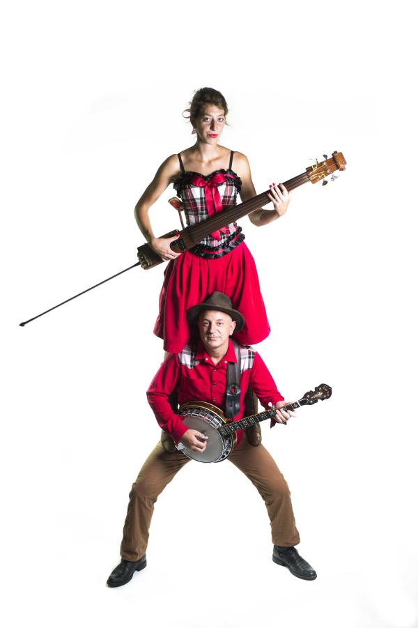 The duo of Crazy Pony. Frank is stood in a shirt, hat and braces. holding his banjo. Léa is standing on his shoulders in a skirt and corset, whilst holding a skinny violin