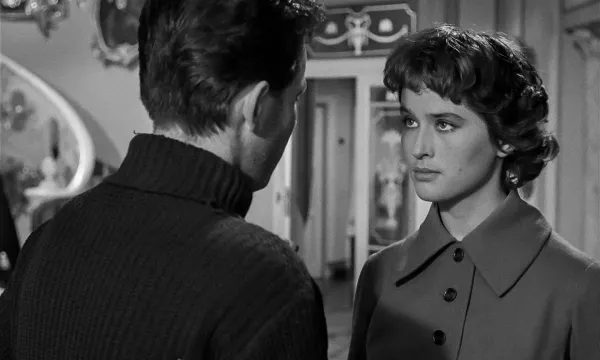 A black and white picture of a man with his back turned to the camera. A woman faced towards the camera is looking at his face.