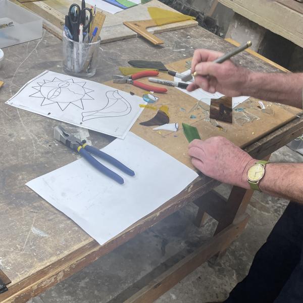 A person cutting out some glass ready to use in a stained glass design