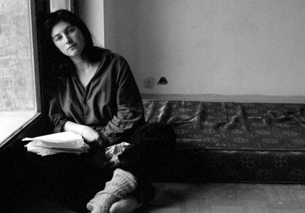 Black and white image of woman on the floor leaning against a window holding sheets of paper.