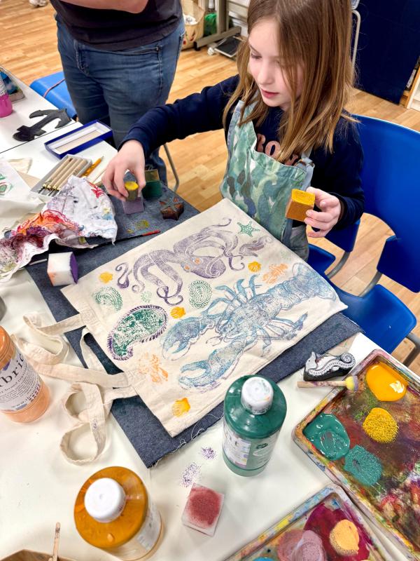 Child works on lino printing tote bag of octopus and other sea creatures.
