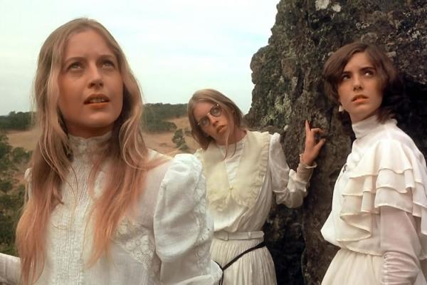Medium shot of three young women next to a rock. They're looking up at something that is out of shot.