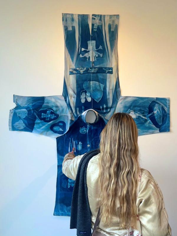 A woman with long hair touches a printed blue garment as it hangs on the wall.