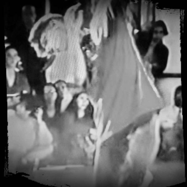 A black and white image of a young dancer looking down at the floor arms raised seemingly pushing away from his face.