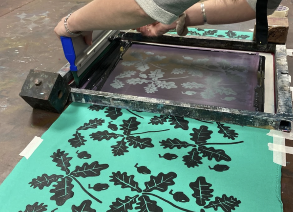 A leaf design in black being screen printed onto green fabric.