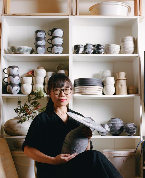 a ceramicist in her studio surround by her work holding a large vase