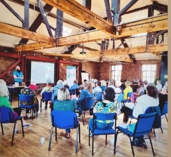 Group of peopl sat in community space big hall with wodden floor and suspended wooden beams