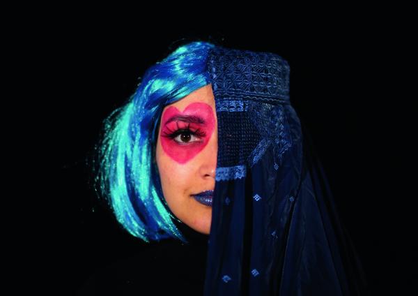 The close-up of half a face with blue hair, blue lipstick and a pink heart drawn around one eye. The other half is covered by a veil.