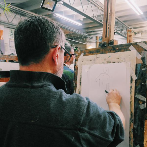The back of a man stood at an easel drawing