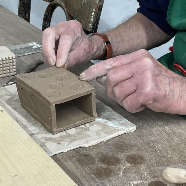 two hand touching a box form made from brown clay