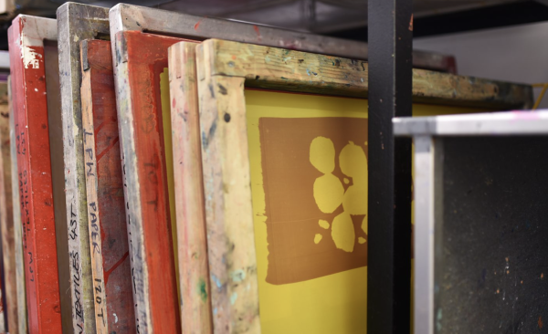 Printing screens with metal and wooden frames being stored in a rack.