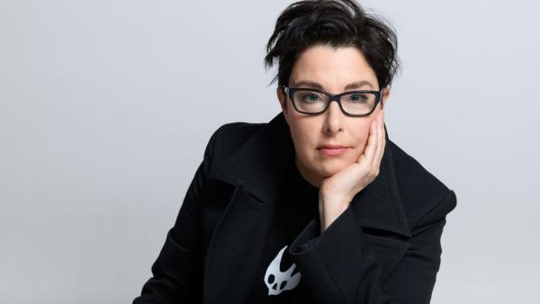 A person with short black hair wearing glasses leaning on their hand.