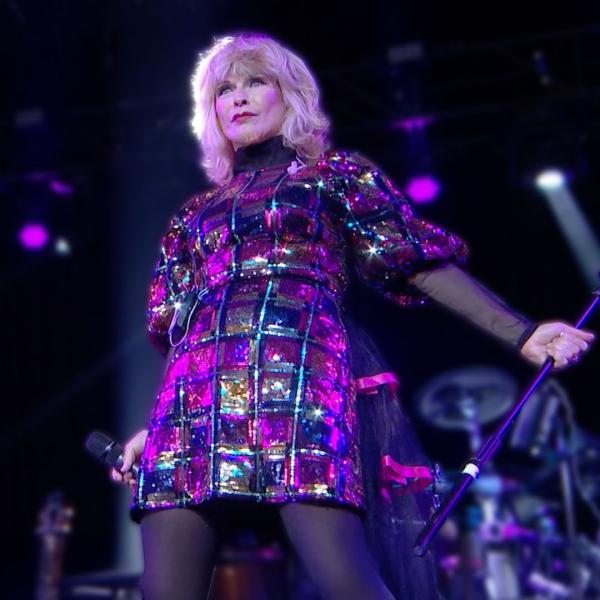 Toyah on stage in a pinky-purply shiny dress pushing a microphone stand out to the side.