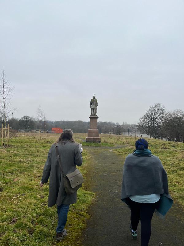 Heritage walkers on Monument Moor in Leeds, walking towards the statue of Henry Rowland Marsden. A seagull is sitting on the statue's head.
