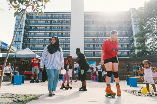 Community members roller skating, playing and chatting at a vibrant outdoor event in Roxby Community Garden, Leeds. The garden is filled with families, children and volunteers taking part in Mafwa Theatre’s Refugee Week celebration in Lincoln Green.