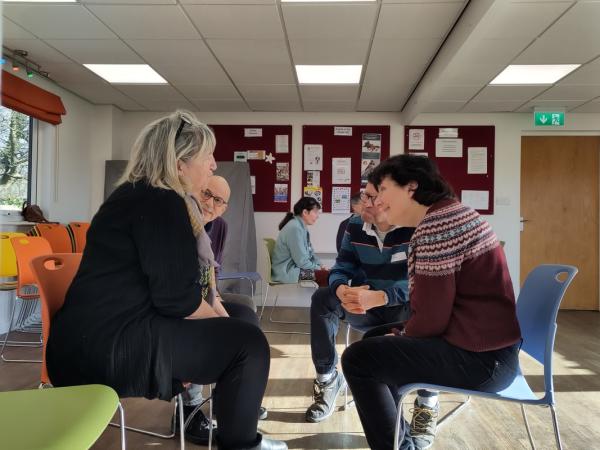 Four people sitting opposite each, they are talking and have smiles on their faces.