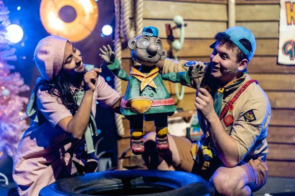 Two actors dressed as children hold a puppet of a third child character