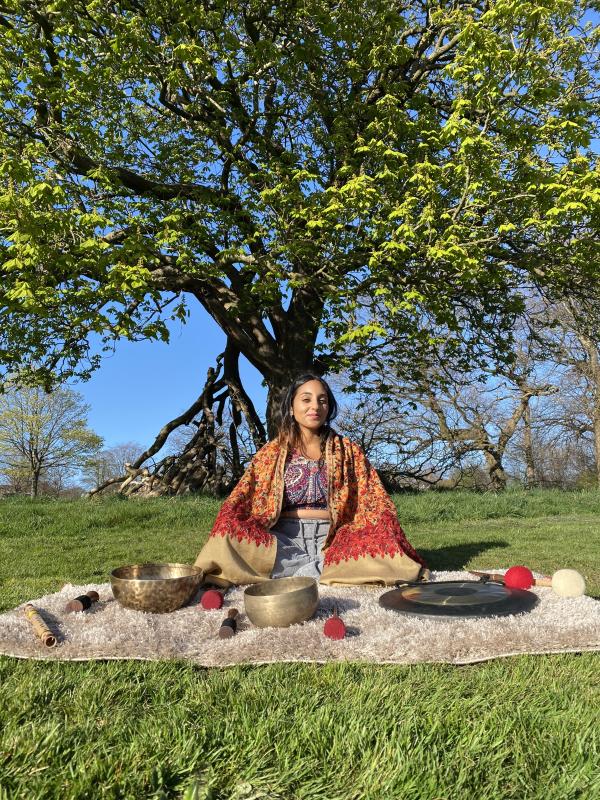 Neeta Sarl sitting beneath a tree with a selection of sound healing instruments