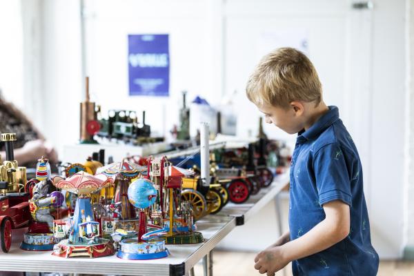 A small boy with blonde hair looking at a table full of steam toys