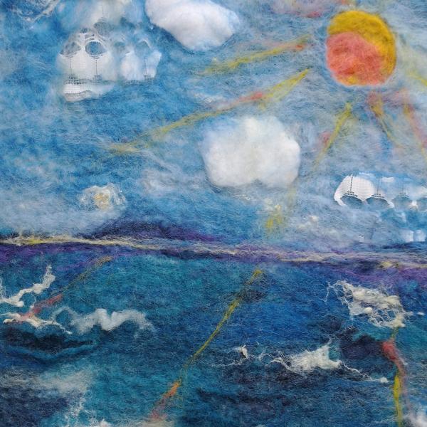 A close up photograph of a felted sunshine over a blue sky and blue sea