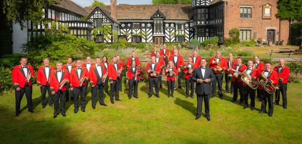 A brass band standing on the green lawn with a country house behind them.  