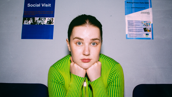 A young woman resting her head on her hands in a prison waiting room.