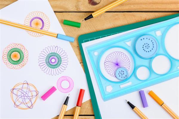 A photo of a spirograph on a table, alongside some pens and paper
