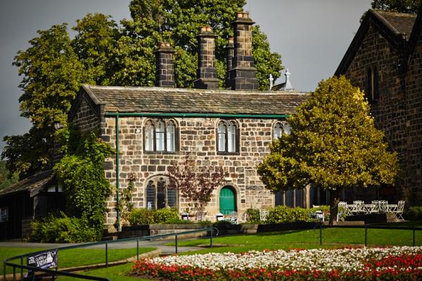 An image of a stone house on a hill. The window frames and doors are painted green. there are trees in the foreground and background and the sky is grey.