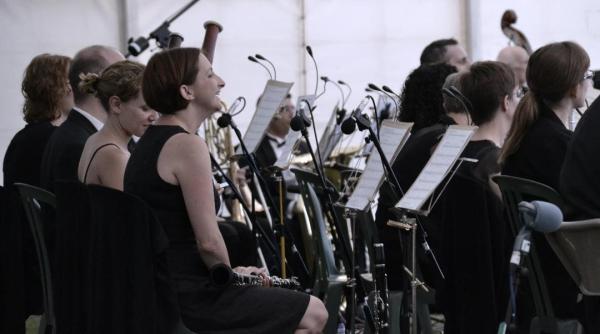 Several people, dressed in black, with musical instruments and music playing in an orchestra
