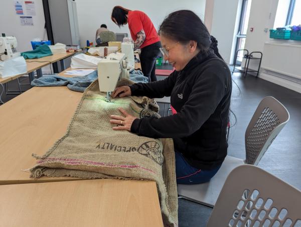 A women sat sewing a bag. 