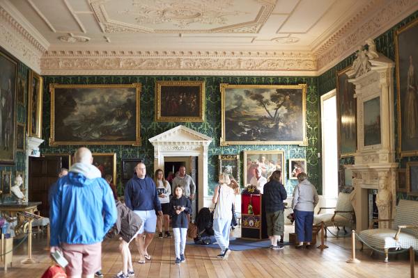 A number of people visiting Temple Newsam in a highly decorated room with lots of paintings and fine furniture on display.
