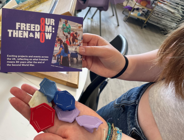 Hands holding a purple postcard and multicoloured paperpieced fabric.